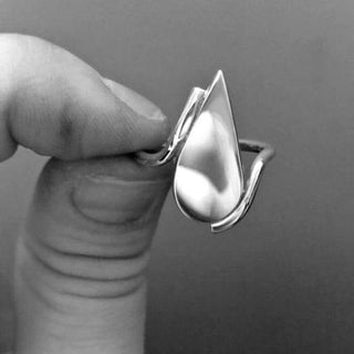 A close-up of a hand holding a silver ring shaped like a droplet, showcasing its elegant design.