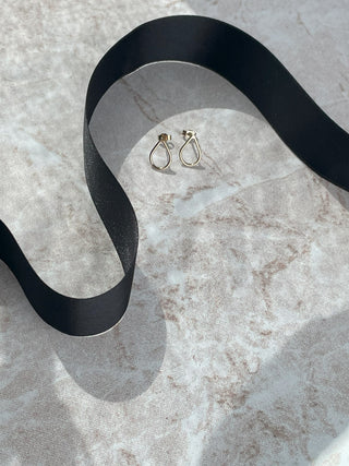 A pair of small gold hoop earrings placed on a light marble surface with a flowing black ribbon behind them.