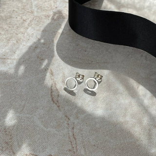 Silver earrings on a textured surface with a black ribbon