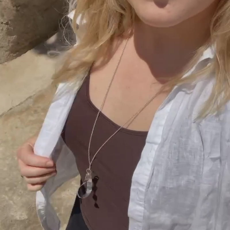 A silver teardrop-shaped pendant necklace with a hammered finish, shown on a moving woman in the sunshine. 