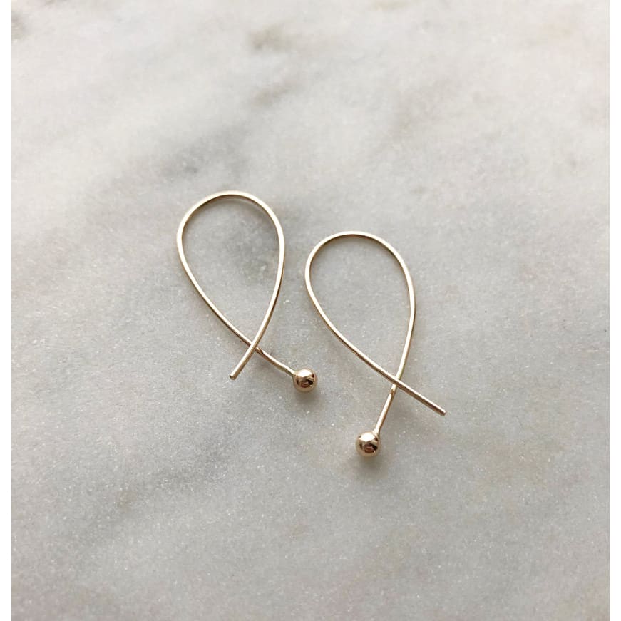 Gabrielle cross over gold earrings by M of Copenhagen placed on marble