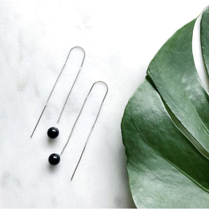 Orbit earrings by M of Copenhagen made with sterling silver and natural onyx beads laid out on marble