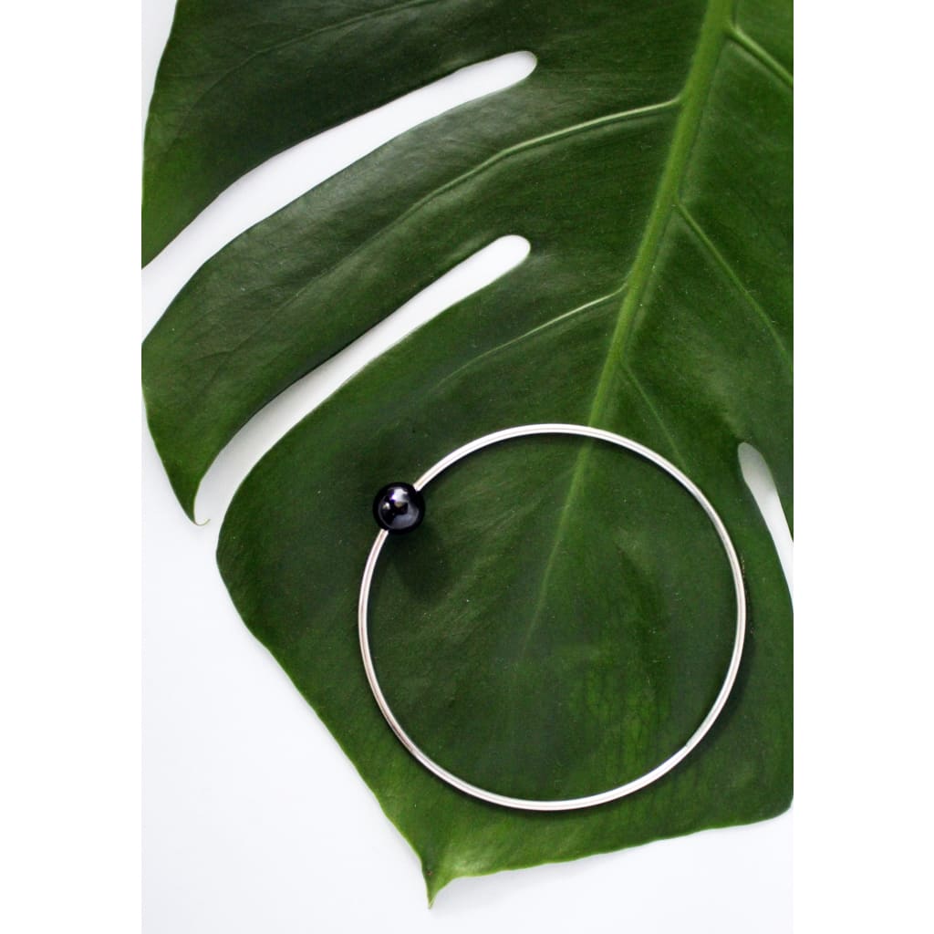Positano bangle by M of Copenhagen made with silver and a natural obsidian bead posed on leaf